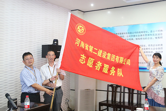 董事長黃道元向黨委副書記陳百斌授志愿者服務(wù)隊(duì)旗